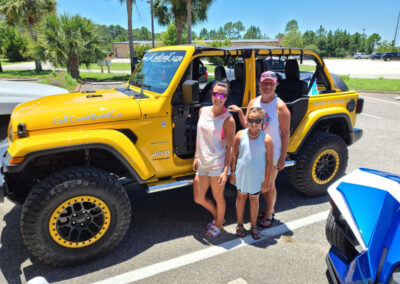 father, mother, daughter standing in front of yellow jeep wrangler